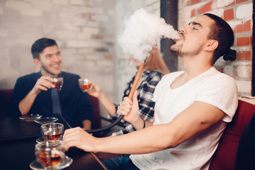 Hookah smoking shisha in bar and nightclub, team of friends laugh, talk and drink Arabic tea