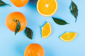 Slices of orange with leaves on blue background. Flat lay, top view.