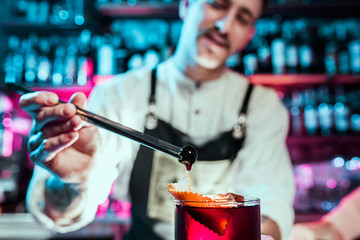 Expert barman is making cocktail at night club or bar. Glass of fiery cocktail on the bar counter against the background of bartenders hands with fire. Barman day concept