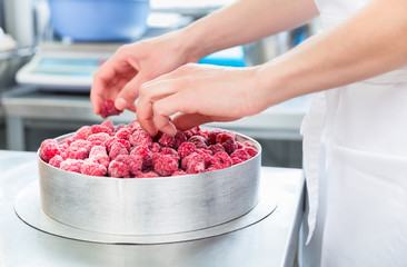 Woman confectioner making raspberry cake in bakery