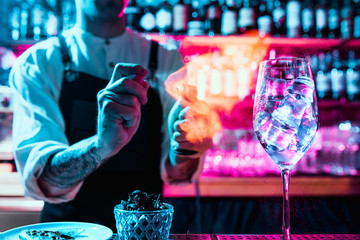 Expert barman is making cocktail at night club or bar. Glass of fiery cocktail on the bar counter against the background of bartenders hands with fire. Barman day concept - obrazy, fototapety, plakaty