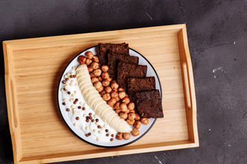 Healthy breakfast on the kitchen table. Rye bread, banana, grains, hazelnut and yogurt on black background