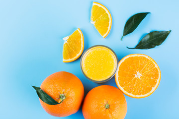 Orange juice in glass and slices of orange on blue background, top view
