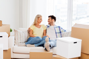 Fototapeta na wymiar mortgage, moving and real estate concept - happy couple with boxes resting on sofa at new home