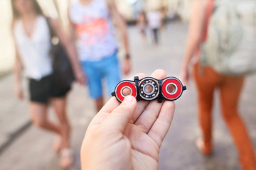 Closeup of hand of kid playing modern popular hand toy spinner made by himself by using screw-nuts and bearing. Child holding unusual metal spinner at blurry people in the street background.