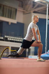 Fototapeta premium Young active man with prosthesis in right leg doing stretching exercise during workout on stadium