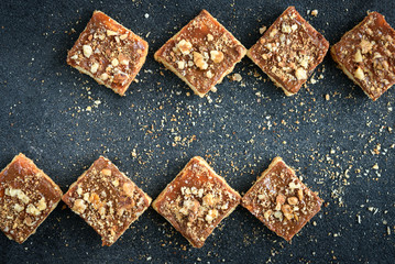 Homemade caramel shortbread squares cookies with nuts laid in the shape of a square on black background with crumbs.