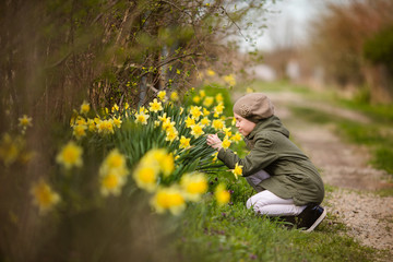 Teenager girl in green jacket and khaki beret near the daffodils' garden in the country. Spring farm and Easter theme