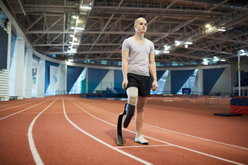 Obraz premium Young sprinter with handicapped right leg standing by start line on race track before marathon on stadium