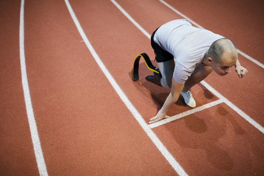 Young runner with handicapped right leg bending over start line on stadium ready to run marathon