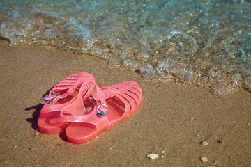 Fototapeta na wymiar Pink Women's JELLY SANDALS on a sea shore. LADIES FLAT JELLIES SUMMER BEACH SHOES. Sand background