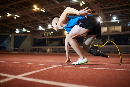 Young man with artificial leg leaning over race track while standing by start line and waiting for signal to go