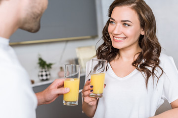 selective focus of attractive woman smiling while holding glass with orange juice near boyfriend