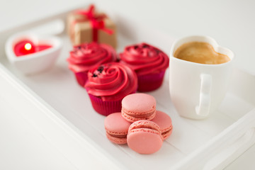Obraz na płótnie Canvas valentines day and sweets concept - close up of pink macarons, cupcakes with red buttercream frosting, heart shaped coffee cup, candle and gift box on tray