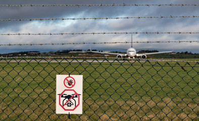 No drone sign on fence of airport runway, Passenger aircraft taxiing on runway in the background