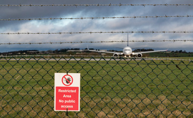 Restricted area sign on fence of airport runway, Passenger aircraft taxiing on runway in the...