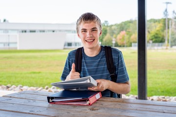 Happy teenager doing his homework outdoors next to a school.