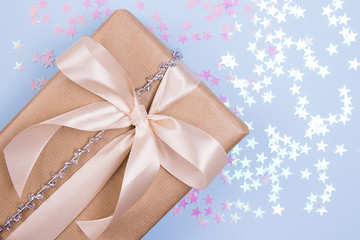 Holidays gift with beige bow and glitter stars on a pastel blue background.