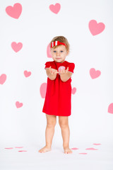Little blonde girl in red dress with red wreath with heatrs on the white background with pink hearts on the St. Valentine's day