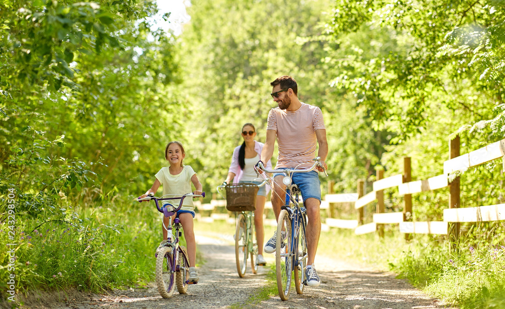 Wall mural family, leisure and people concept - happy mother, father and little daughter riding bicycles in summer park