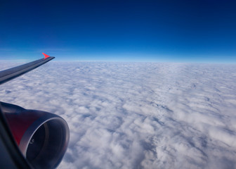 View of wing and turbine of an passenger  airplane flying above the clouds, morning time. Clouds and sky through an airplane window