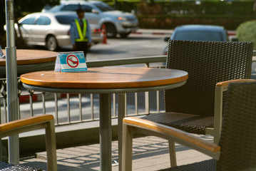 Selective focus on non-smoking sign on the wooden vintage table and vacancy chairs at the terrace of coffee shop in the afternoon