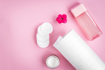 Face hygiene. Towel, tonic, cream, cotton pad and flower on pink background. 