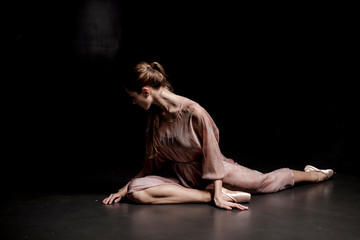 Fototapeta na wymiar Tired ballerina sitting on stage on black background close up