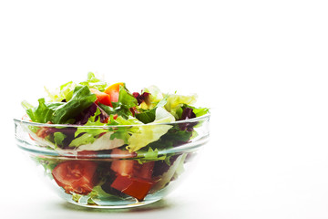 various fresh mix salad leaves with tomato in glass bowl isolated on white background.