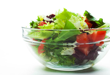 various fresh mix salad leaves with tomato in glass bowl isolated on white background.