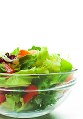 various fresh mix salad leaves with tomato in glass bowl isolated on white background.