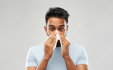 health problem, rhinitis and allergy concept - unhealthy indian man with paper napkin blowing nose over grey background - obrazy, fototapety, plakaty