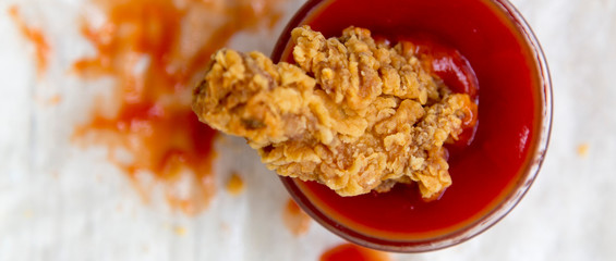 Fried chicken wing in a bowl of ketchup, top view. From above, overhead.