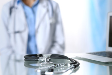 Stethoscope lying on glass desk with laptop computer at busy physician background. Medicine or pharmacy concept. Medical tools at doctor working table
