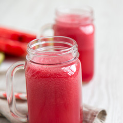 Watermelon smoothie in glass jars on a white wooden background, side view. Closeup.