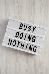 Modern box with text 'Busy doing nothing' on a white wooden surface, top view. From above, flat lay, overhead.