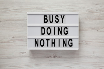 Lightbox with text 'Busy doing nothing' on a white wooden background, top view. From above, flat lay, overhead.