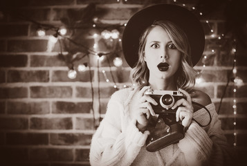 Portrait of a young cozy woman in white sweater with vintage camera and Christmas lights and pine branch
