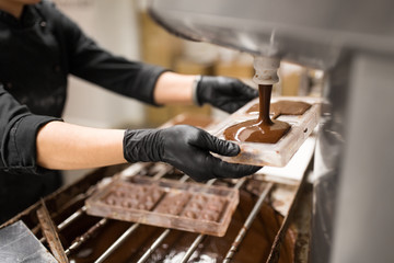 production, cooking and people concept - confectioner filling candy mold with chocolate at...