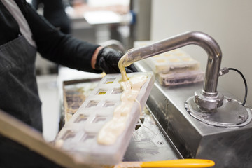 production, cooking and people concept - confectioner filling candy mold with white chocolate at confectionery shop
