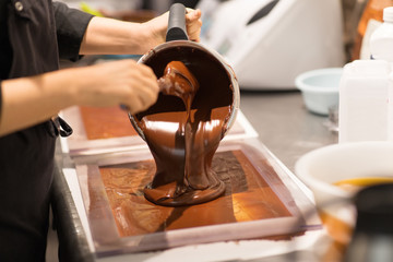 production, cooking and people concept - confectioner filling mold with chocolate at confectionery...