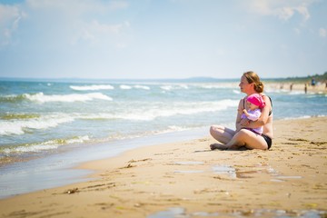 Fototapeta na wymiar Mother with small baby girl relaxing on sea beach