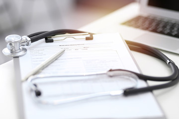 Stethoscope, clipboard with medical form lying on hospital reception desk with laptop computer. Medical tools at doctor working table.Medicine and health care concept