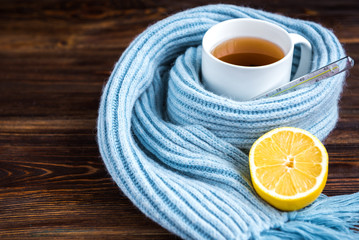 Tea cup with thermometer, blue scarf and lemon on wooden background. Flu season, disease.