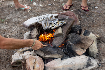 friends party grilled squid, shell seafood with fire outdoor. cooking time in nature with fresh food in island beach.