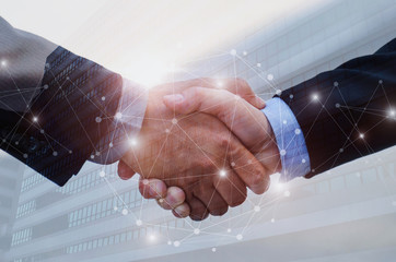 double exposure of business man handshake on modern office building background with network...