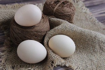  Three Easter eggs and brown threads lie on a beige napkin on a dark background.