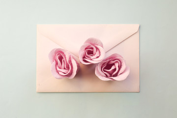 white envelope, three pink rose flowers on a blue background. Minimal Flat lay