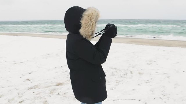 Young beautiful woman taking pictures of the sea on a cold winter day. Slow motion 
