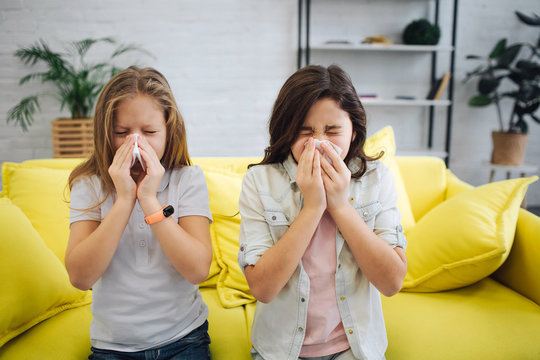 Two sick teenagers stand in room and sneeze. They hold white tissues in hands. Gitls suffer. They sick.